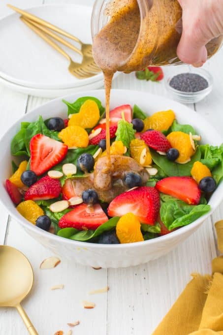 Pouring a poppy seed dressing onto a spinach salad.